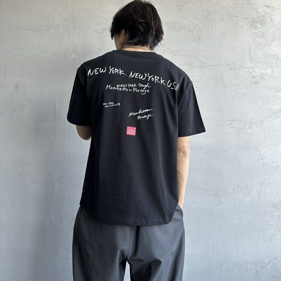 MANHATTAN PORTAGE [マンハッタンポーテージ] 別注 ランダムロゴ バックプリントTシャツ [25SSMP-IN66-JF] BLACK &&モデル身長：179cm 着用サイズ：L&&