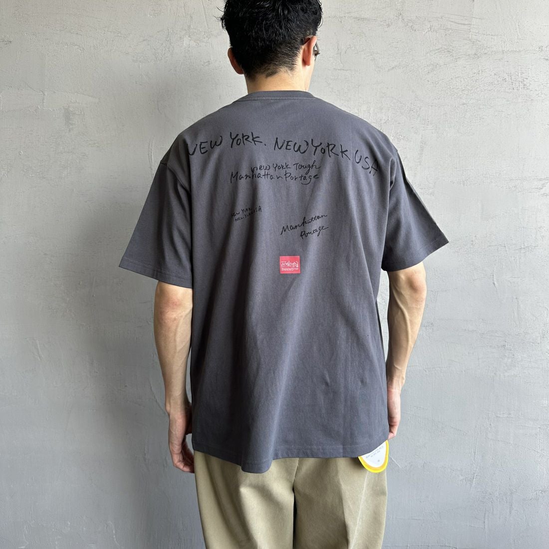 MANHATTAN PORTAGE [マンハッタンポーテージ] 別注 ランダムロゴ バックプリントTシャツ [25SSMP-IN66-JF] CHARCOAL &&モデル身長：168cm 着用サイズ：L&&