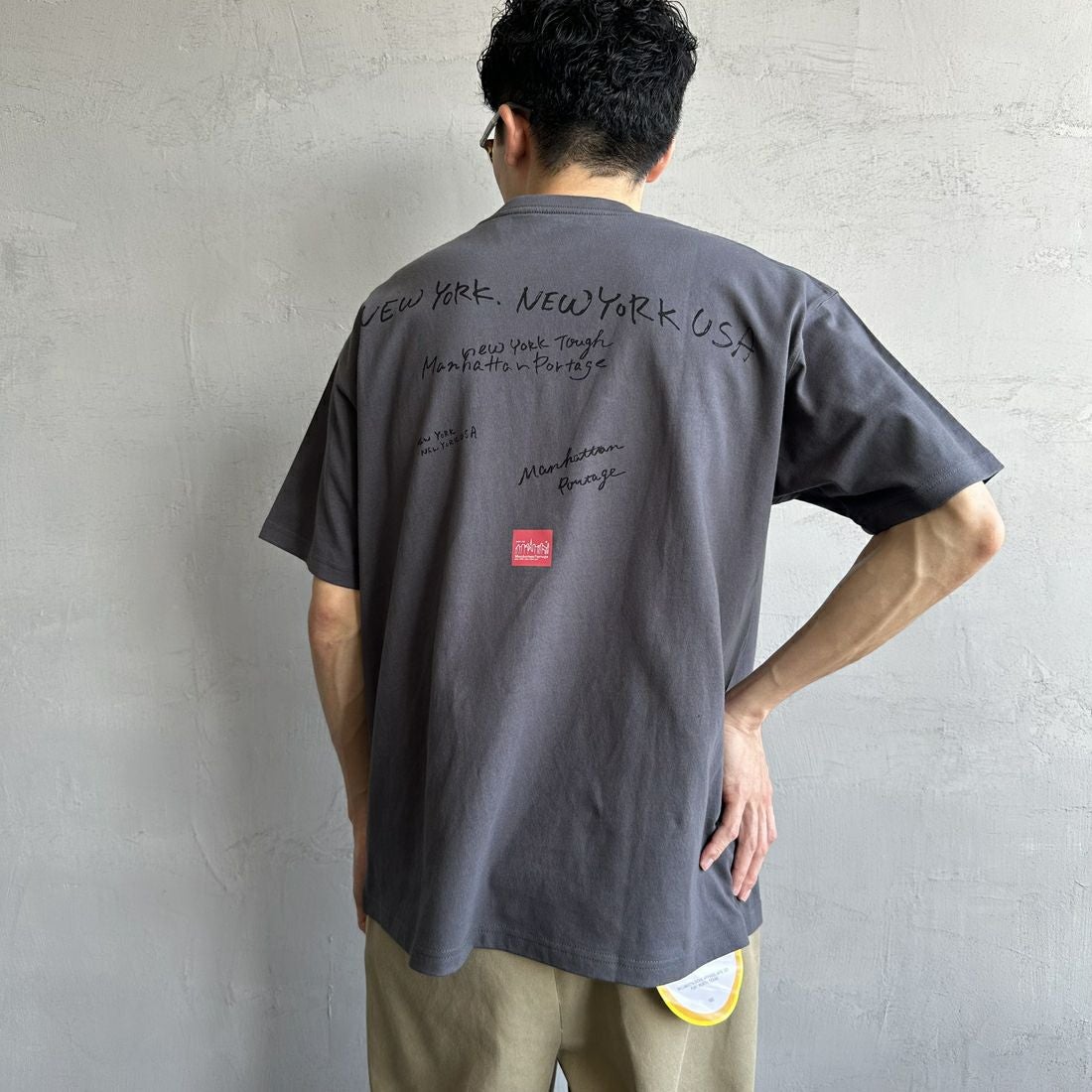 MANHATTAN PORTAGE [マンハッタンポーテージ] 別注 ランダムロゴ バックプリントTシャツ [25SSMP-IN66-JF] CHARCOAL &&モデル身長：168cm 着用サイズ：L&&