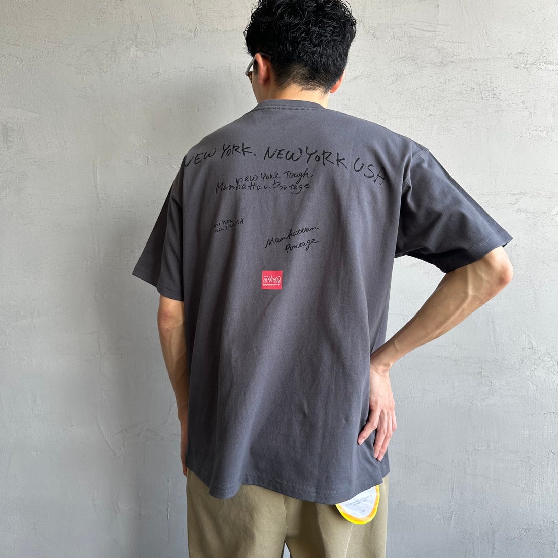 MANHATTAN PORTAGE [マンハッタンポーテージ] 別注 ランダムロゴ バックプリントTシャツ [25SSMP-IN66-JF] CHARCOAL &&モデル身長：168cm 着用サイズ：L&&